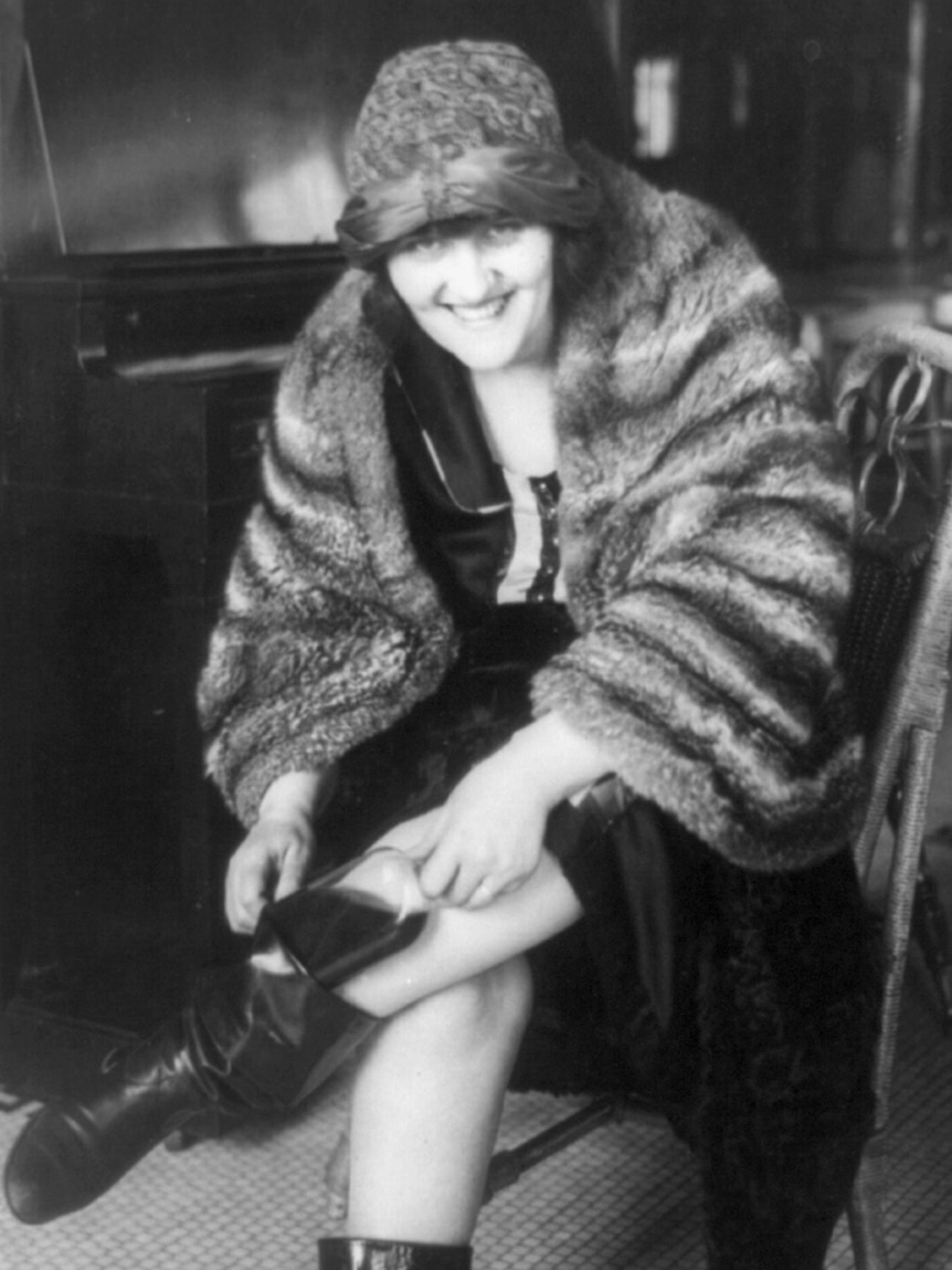 A black and white photo of a 1920s woman putting a flask in her boot.