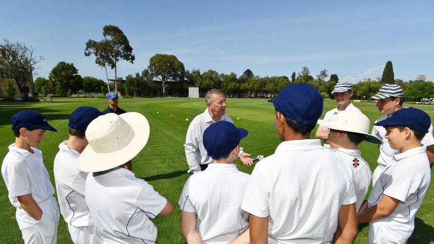 Rod Marsh talks to a group of junior cricketers circled around him on a cricket field