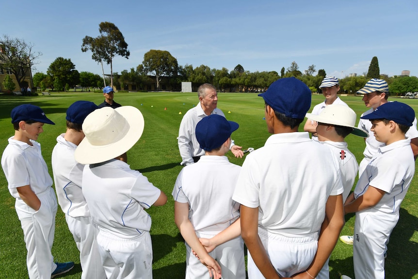 Rod Marsh talks to a group of junior cricketers circled around him on a cricket field