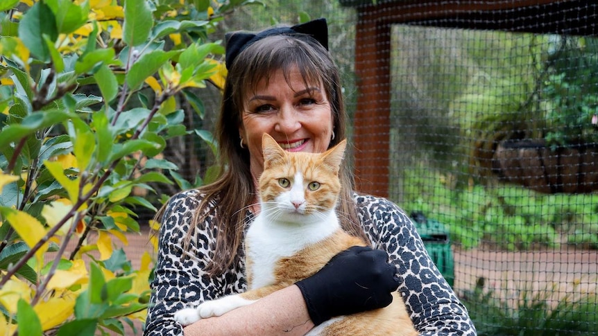 A woman holding a cat inside an enclosure.