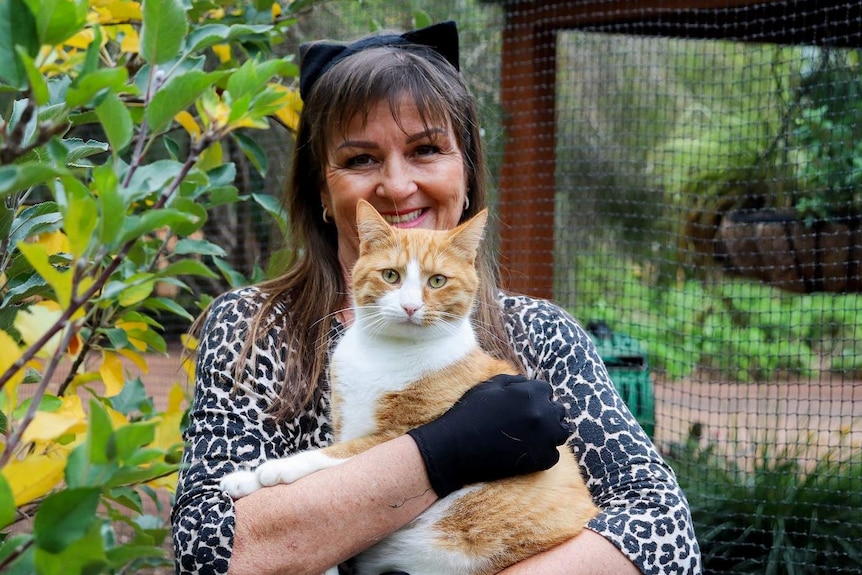 A woman holding a cat inside an enclosure.