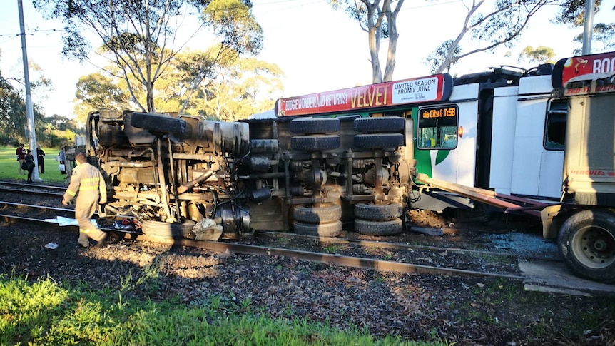 A truck lies on its side over tram tracks beside a derailed tram in Parkville.