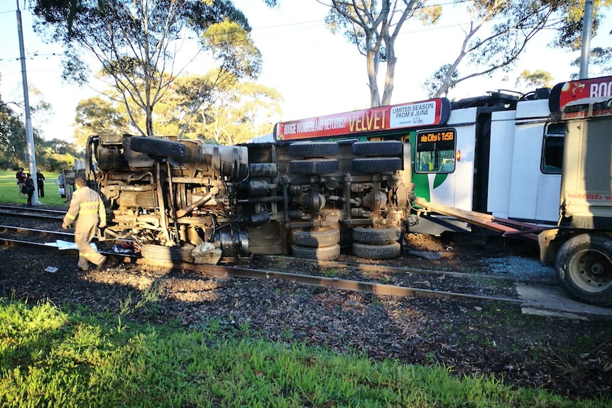 A truck lies on its side over tram tracks beside a derailed tram in Parkville.