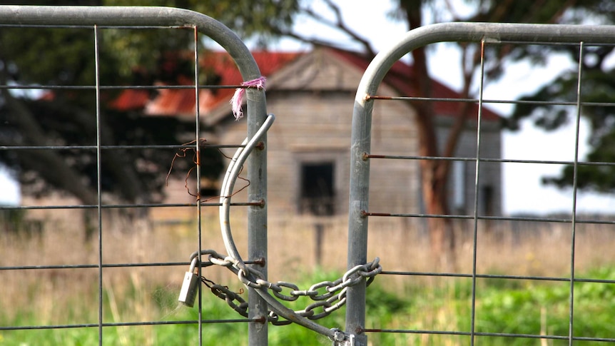 A locked farm gate with abandoned house in the background