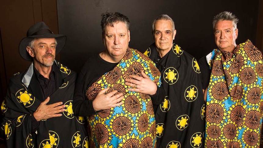 Four members of Sunnyboys wear kaftans with sunflowers and suns printed on them. They stand in a row.