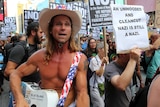 The Naked Cowboy stands next to a protester holding a sign that reads "An unhooded and clean-cut Nazi is still a Nazi".