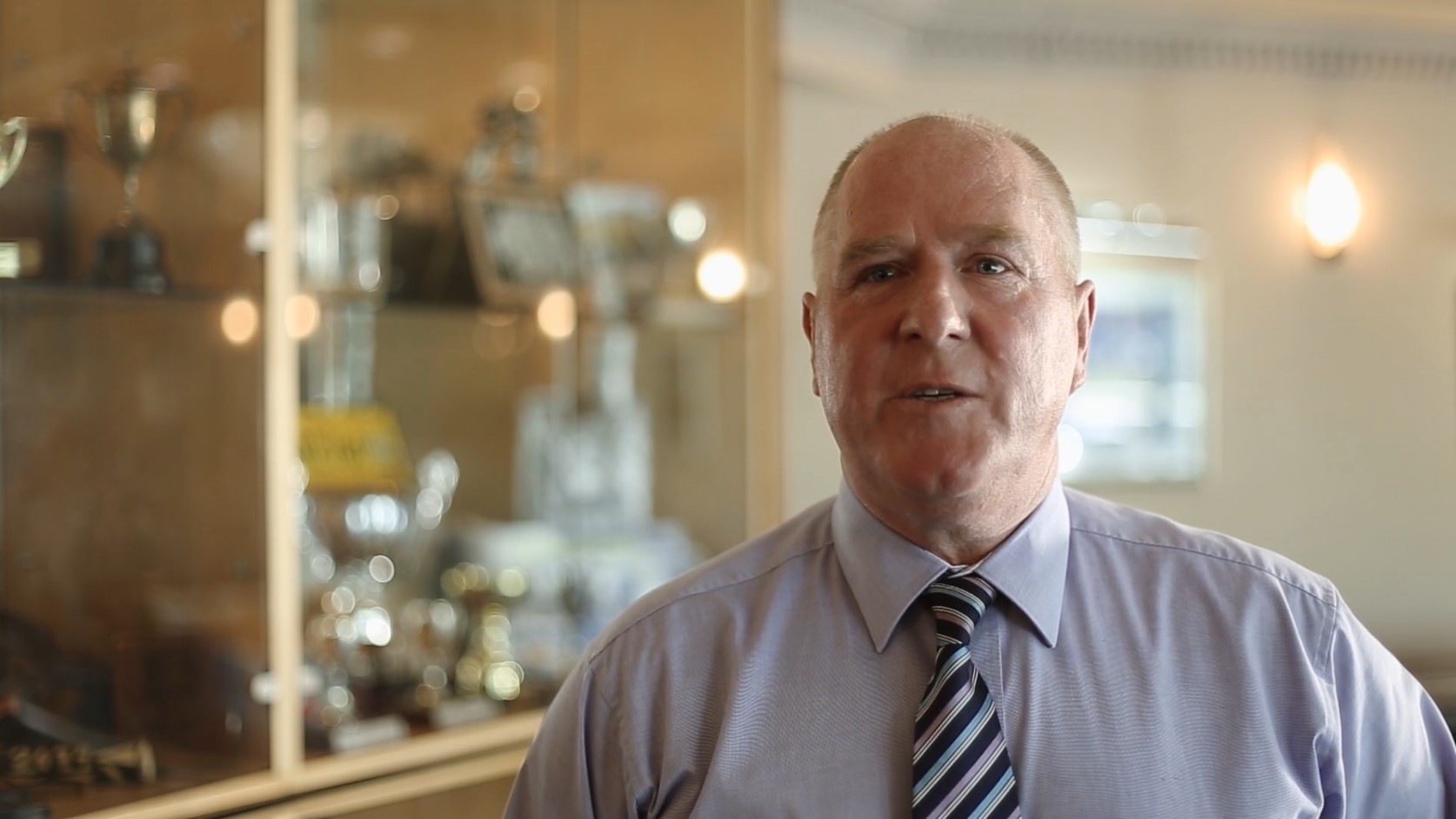 An older man in front of a trophy cabinet.