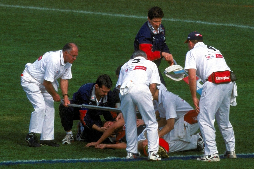 AFL player being attended to by medical staff following a collision during a match