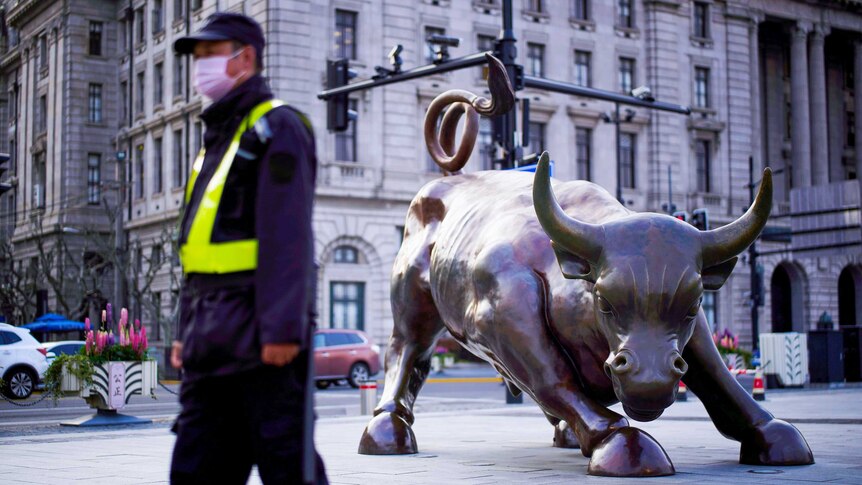 A guard in a face mask walks past a brass bull statue in Shanghai