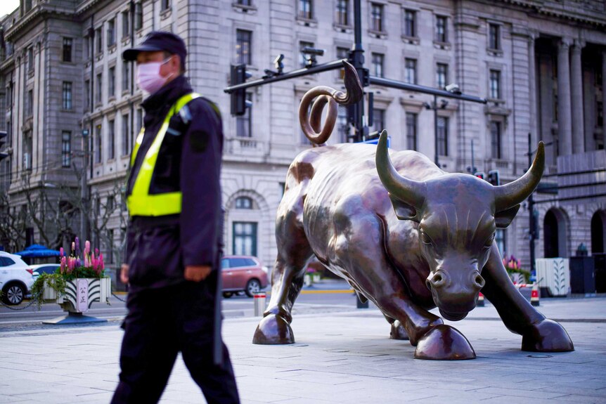 A guard in a face mask walks past a brass bull statue in Shanghai