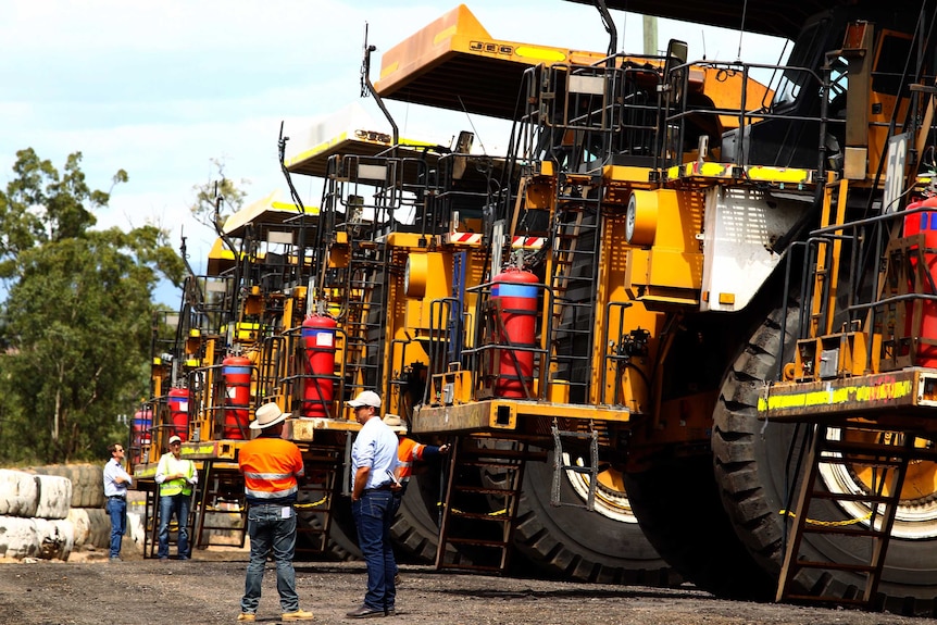 Five large yellow mining trucks in line with two men in foreground