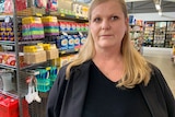 A woman with blonde hair stands in front of a supermarket shelf