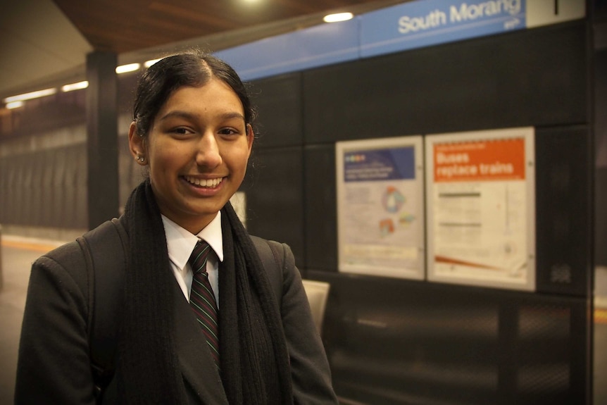 In a dimly-lit new train station platform, you view a young Australian student of South Asian descent in school uniform.