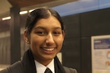 In a dimly-lit new train station platform, you view a young Australian student of South Asian descent in school uniform.