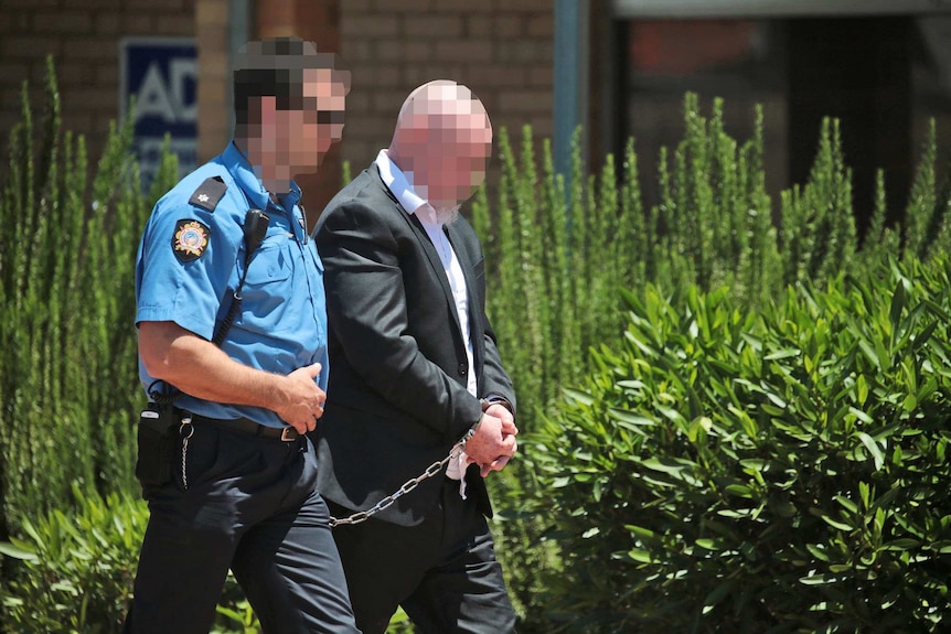 A police officer escorts a hand-cuffed Francis John Wark through the streets of Moora