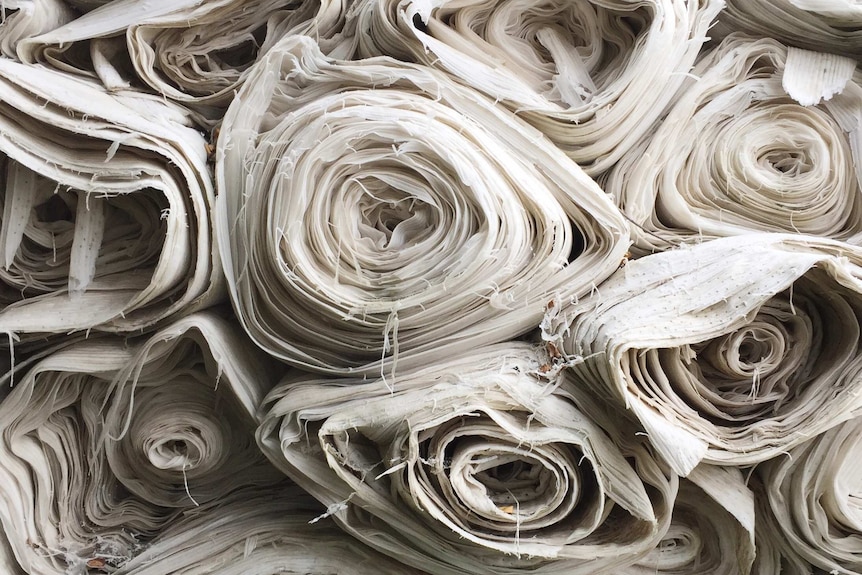 Close up of a large stack of bolts of white fabric.