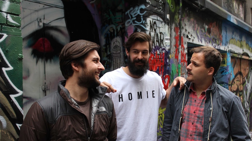 Three men stand in a graffiti covered laneway