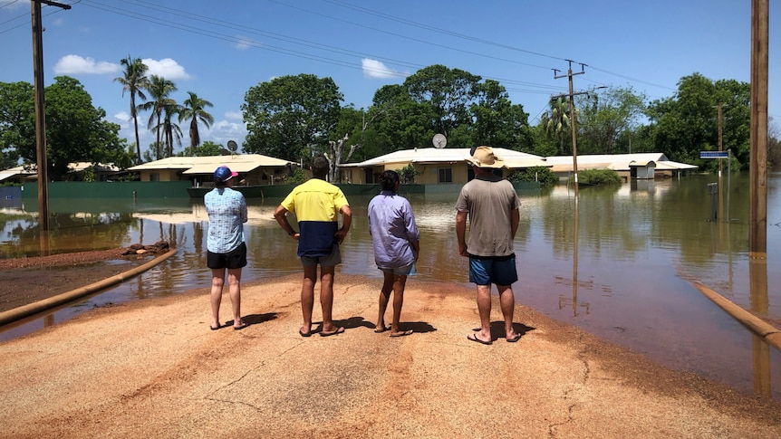 People stand on a street looking at deep floodwaters