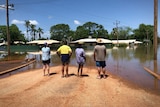 People stand on a street looking at deep floodwaters