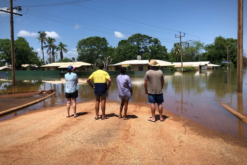 People stand on a street looking at deep floodwaters