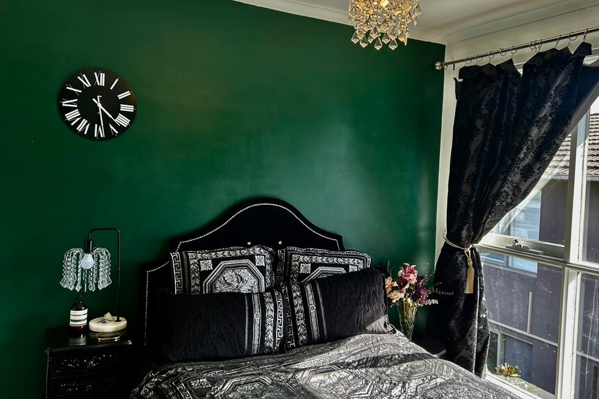A luxurious gothic-style bedroom with deep green-painted walls, a bed with black sheets and headboard, and black curtains.