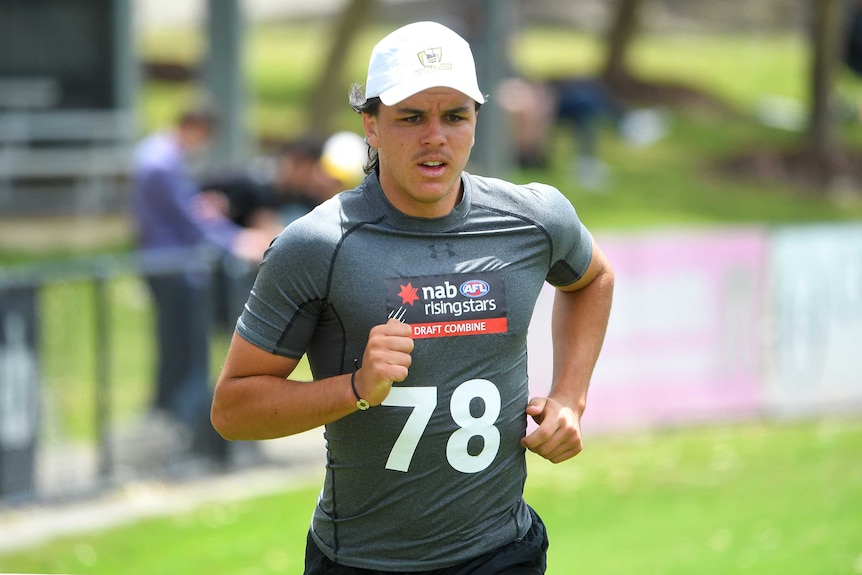 A cap wearing young AFL Draft prospect runs around an oval during training.