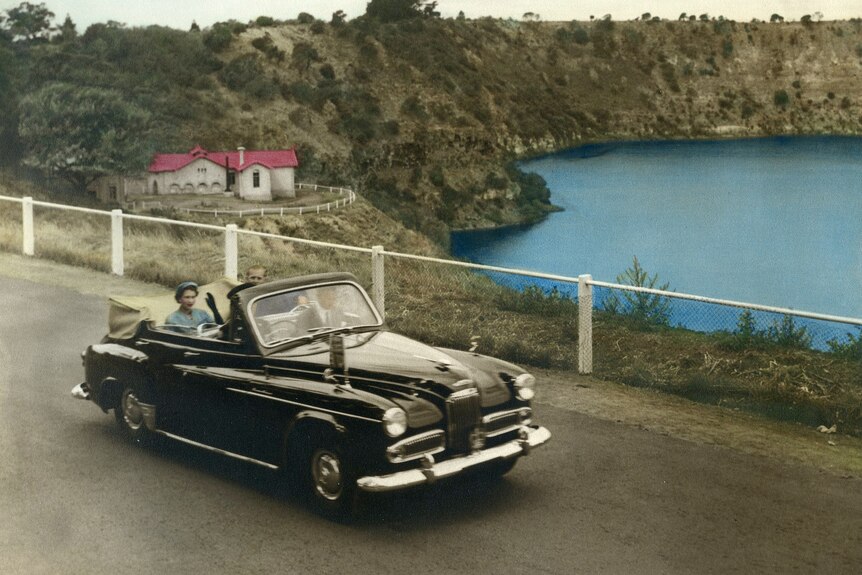 Queen Elizabeth II in the passenger seat of a black car with a Blue Lake behind her.