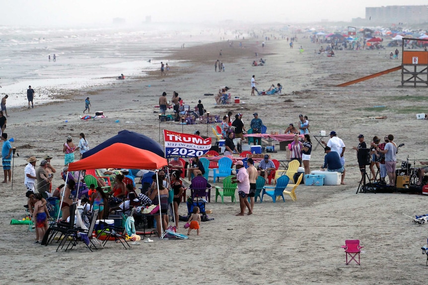 People cluster under marquees on the beach.