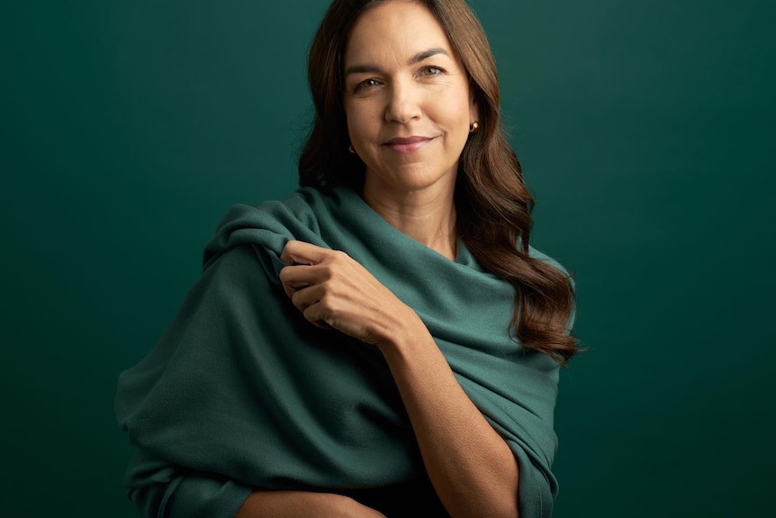 Woman smiling wraped in green outfit with green backdrop. 