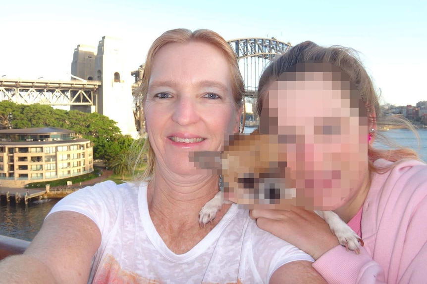 Maree Crabtree takes a selfie with her daughter [whose face is pixelated] and a dog in front of the Sydney Harbour bridge