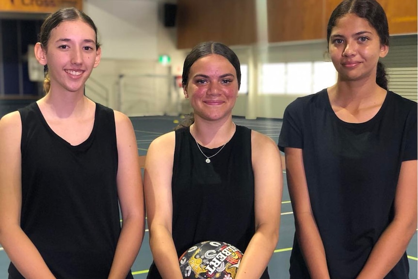 Three young Indigenous netballers smile for a photo