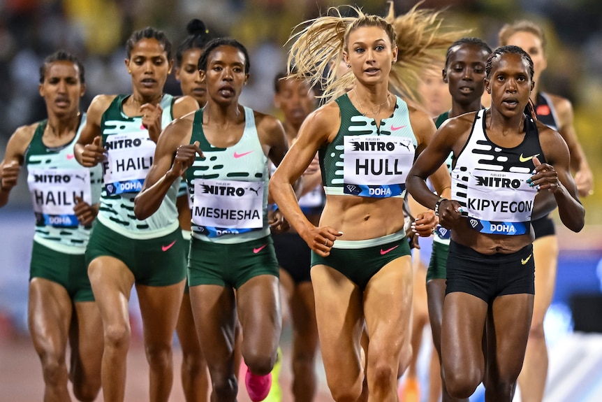 A group of women run around a track.
