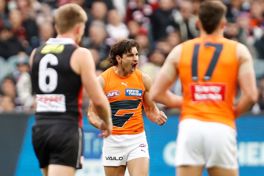 A GWS AFL player roars in celebration and pumps his fists after kicking a goal.
