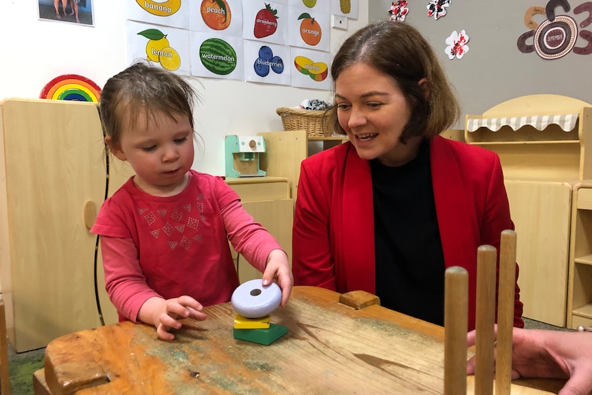 A lady in red and a toddler play with building blocks.