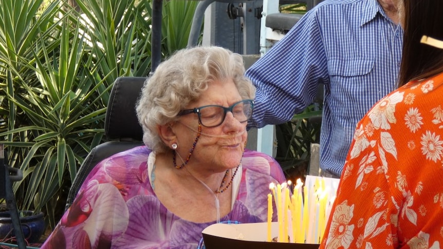 An elderly woman leans in to blow out candles on her birthday cake