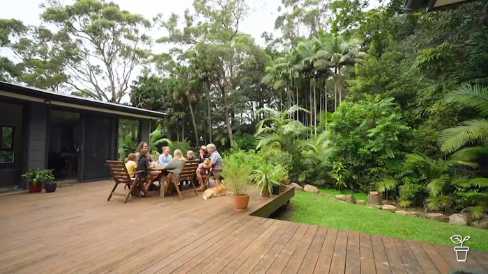 People sitting at an outdoor table on a deck in a garden.