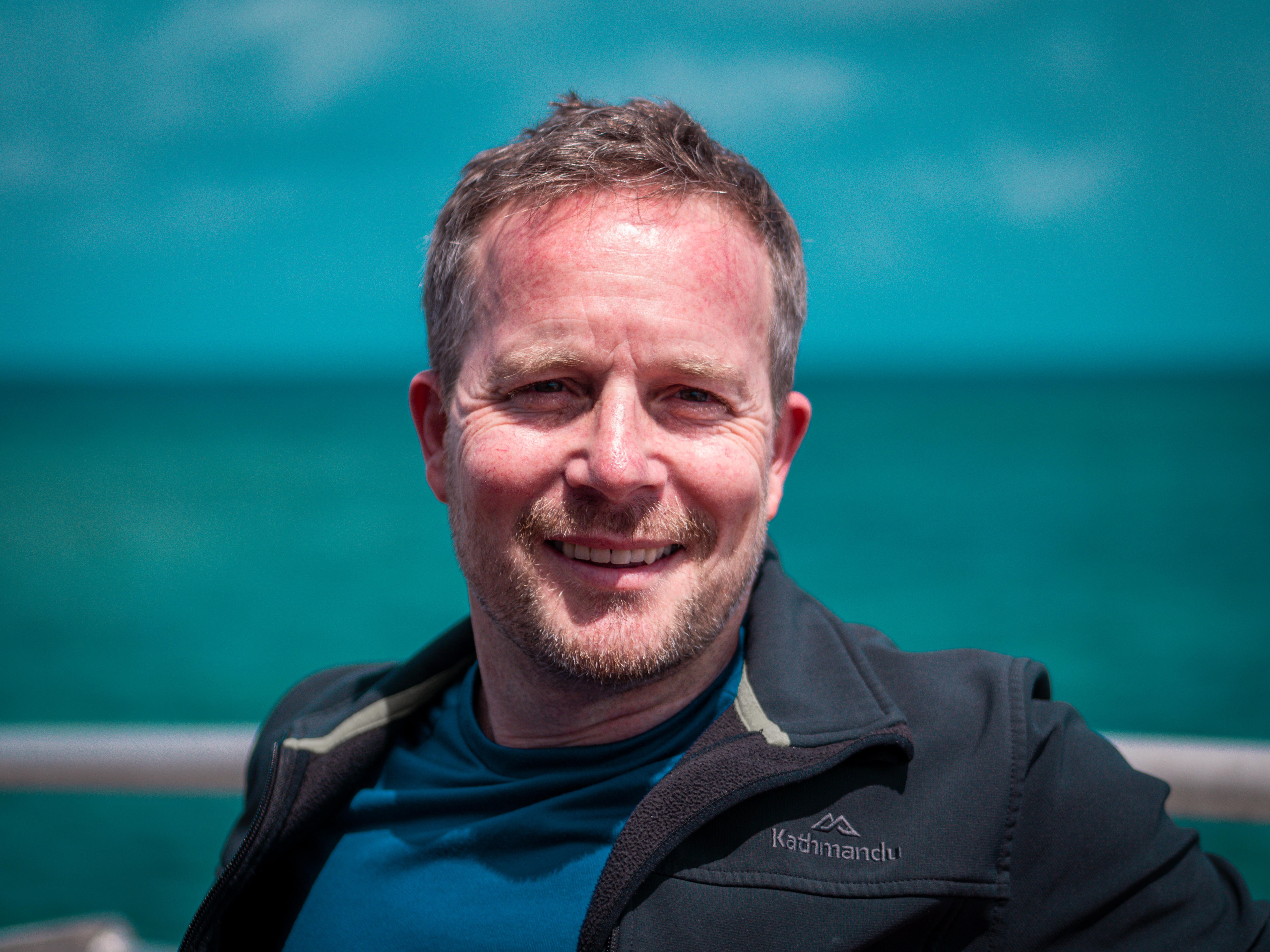 A man in a jacket smiles at the camera.