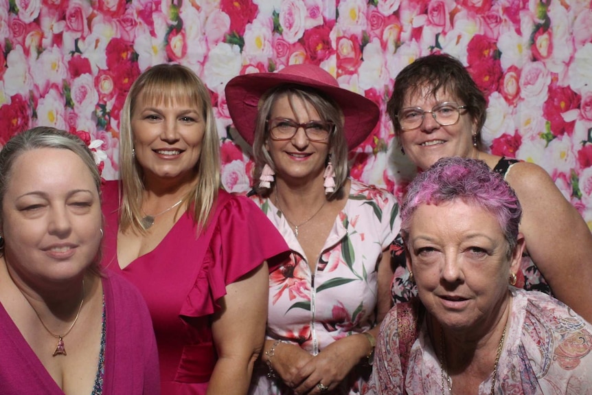 Members of the support group dressed in pink standing in front of floral wall paper