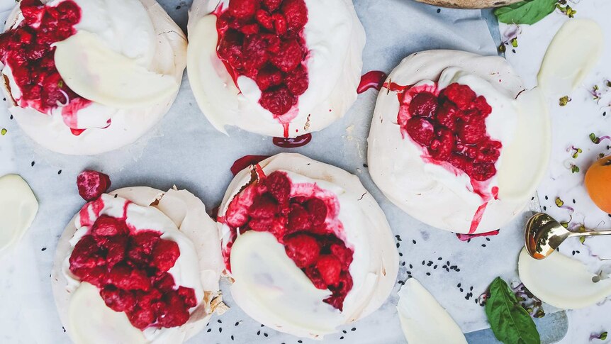 Overhead shot of five small pavlova desserts topped with cream and raspberries.