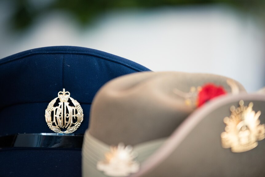 A dark blue hat with a golden RAAF emblem on it, and a beige hat with a curved brim.