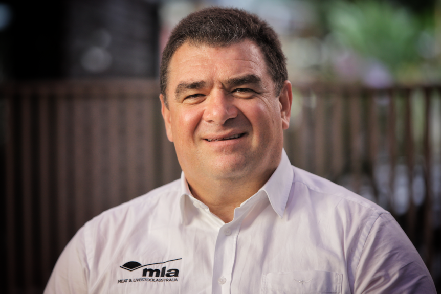A dark-haired, smiling, older man wearing a white collared shirt with the MLA logo on his right chest