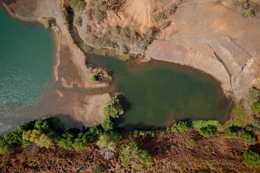 A mine site including a large green body of water and surrounded by trees is viewed from above.