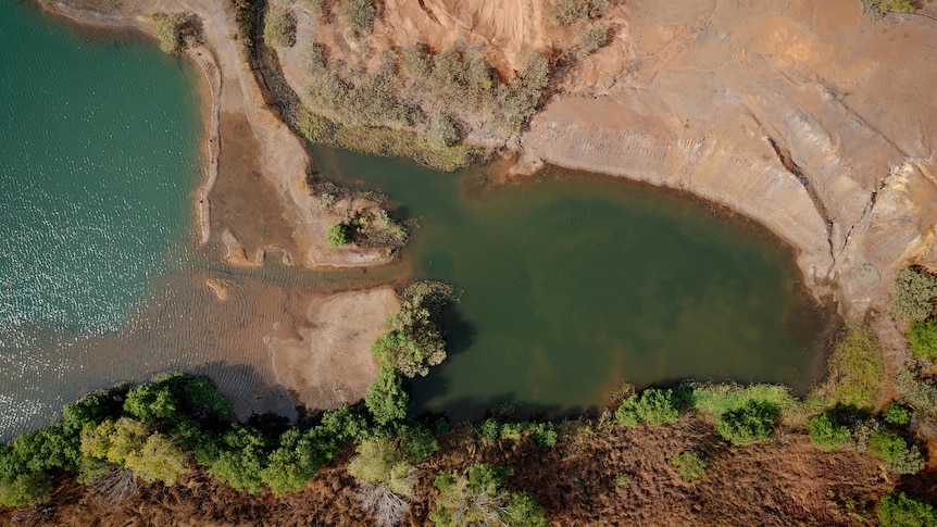 A mine site including a large green body of water and surrounded by trees is viewed from above.