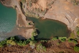 A mine site including a large green body of water and surrounded by trees is viewed from above.