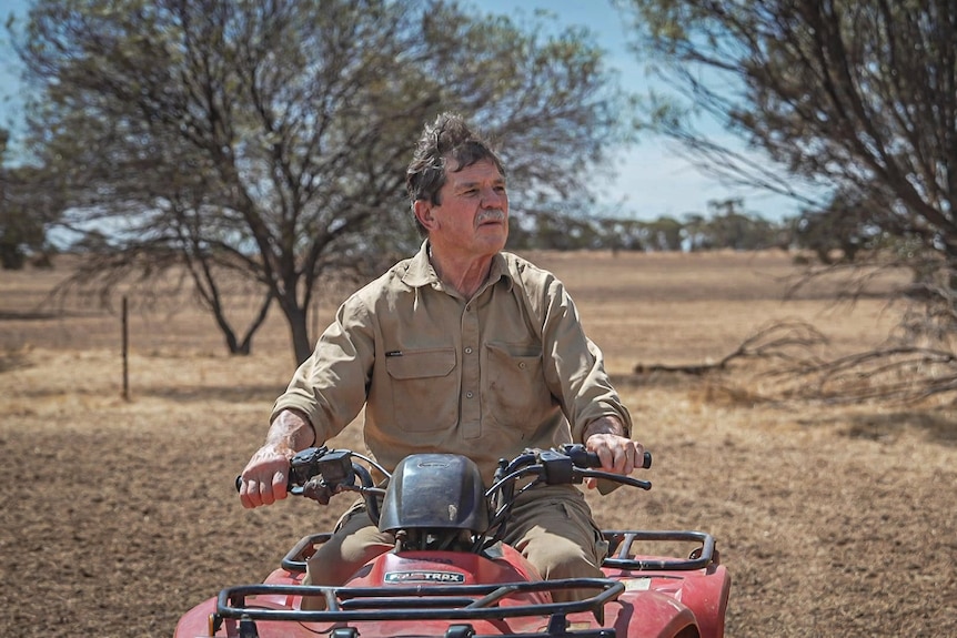 Man with grey hair wearing khaki work gear on red four wheel motorbike