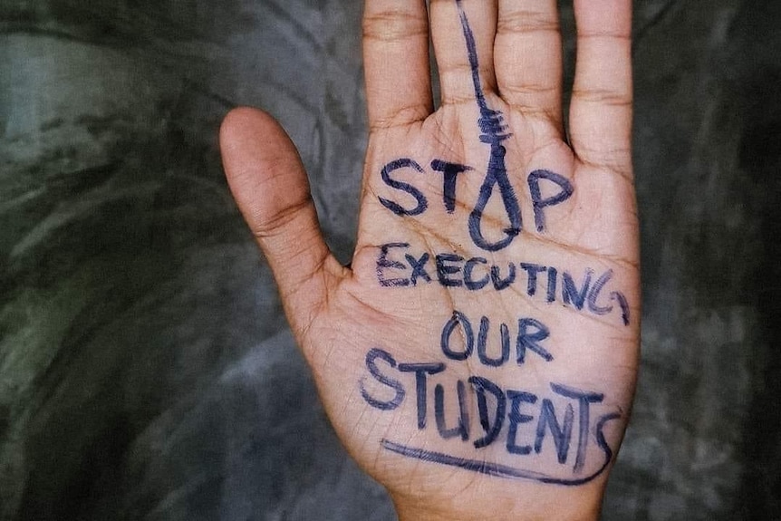 A hand with "stop executing our students" written in pen. The O in STOP is drawn like a noose