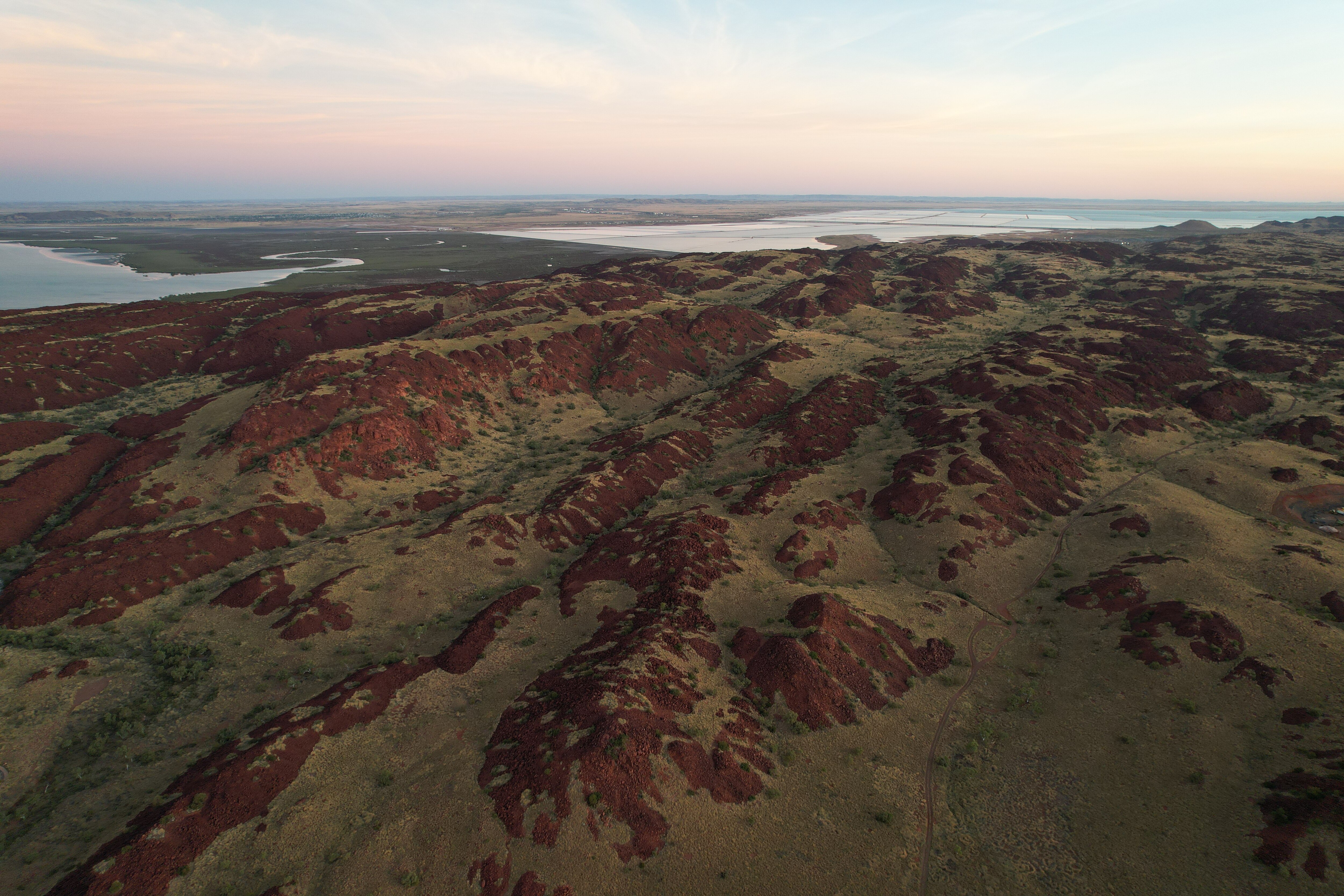 Aerial photo showing green spinifex creeping up deep red rocks with ocean in the background