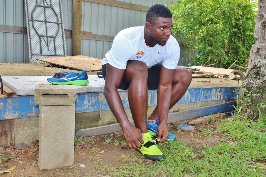 Mustafa puts on his athletic shoes while sitting on a makeshift bench next to a cinder block.