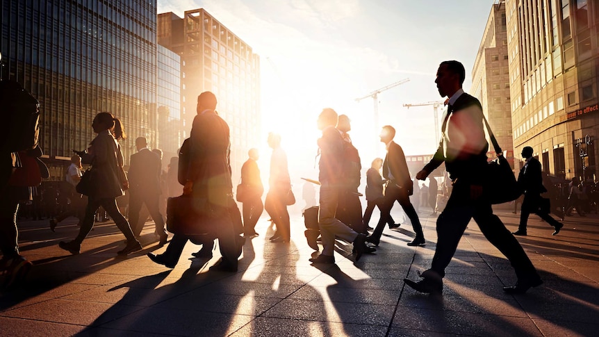 office workers silhouetted against late daylight, crossing a street