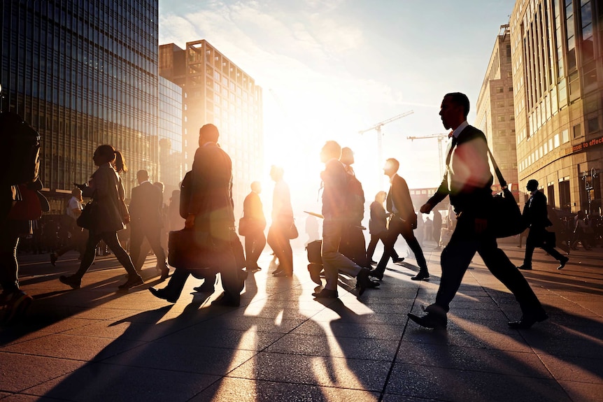 office workers silhouetted against late daylight, crossing a street